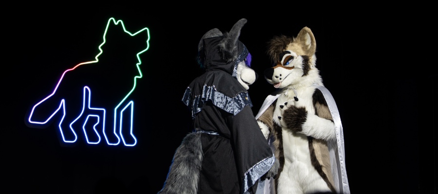 Two fursuiters standing on stage in front of a brightly lit Awoostria logo (wolf going awoo)