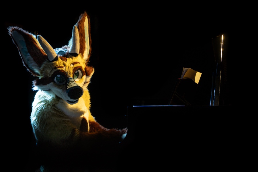 CoVahr, a fox-dragon fursuiter, playing the piano on stage while looking cutely at the camera